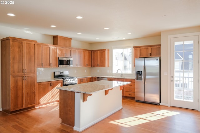 kitchen with a center island, a kitchen bar, stainless steel appliances, sink, and light wood-type flooring