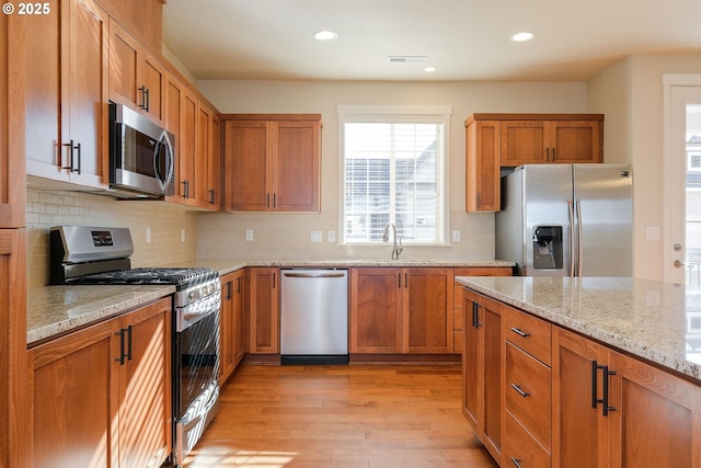 kitchen with sink, backsplash, light stone counters, light hardwood / wood-style floors, and stainless steel appliances