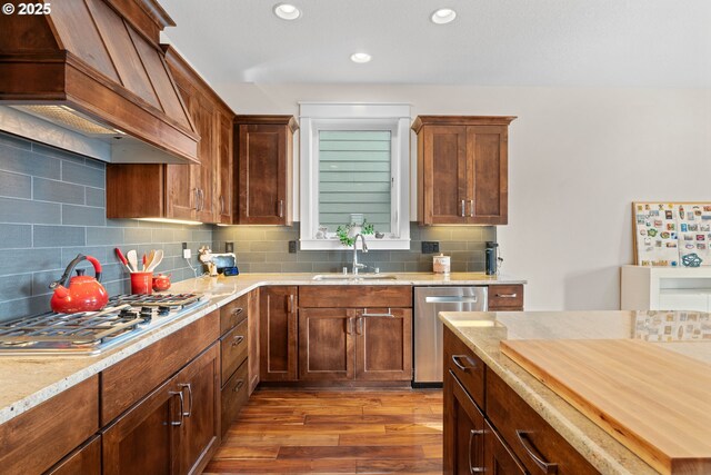 kitchen with wood finished floors, a sink, custom exhaust hood, stainless steel appliances, and backsplash