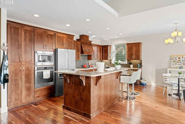 kitchen featuring stainless steel appliances, wood-type flooring, backsplash, and a kitchen breakfast bar