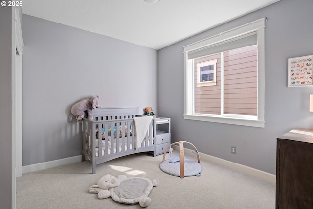 carpeted bedroom featuring a nursery area and baseboards