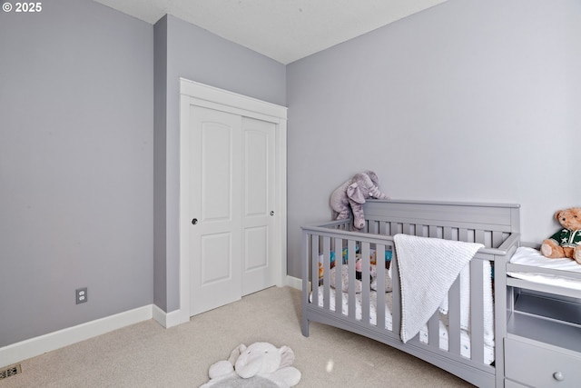 bedroom with a closet, visible vents, carpet flooring, a crib, and baseboards