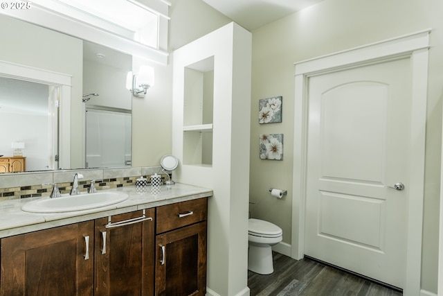 bathroom with toilet, wood finished floors, vanity, baseboards, and backsplash