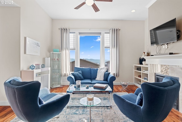 living room with ceiling fan, baseboards, a tiled fireplace, and wood finished floors