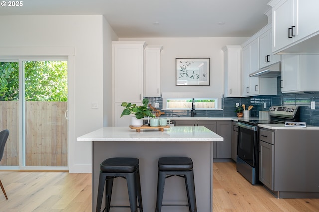 319 N Holland St, Portland, OR 97217 - kitchen featuring stainless steel range with electric stovetop, under cabinet range hood, light wood-style flooring, and a kitchen bar