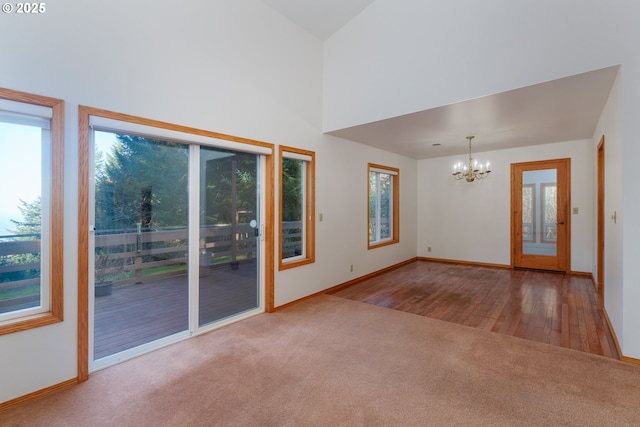 unfurnished living room with an inviting chandelier, plenty of natural light, light carpet, and a high ceiling