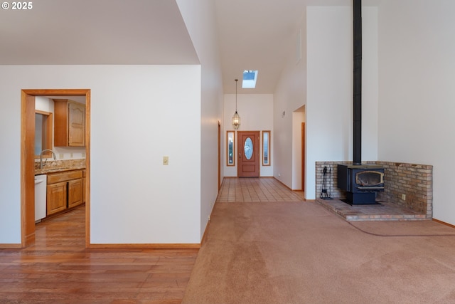 unfurnished living room with high vaulted ceiling, light hardwood / wood-style floors, sink, and a wood stove