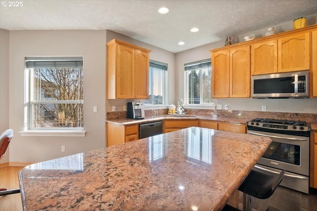 kitchen with a kitchen bar, sink, light stone counters, a textured ceiling, and appliances with stainless steel finishes