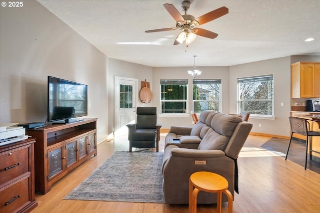 living room featuring ceiling fan with notable chandelier, light hardwood / wood-style flooring, and a textured ceiling