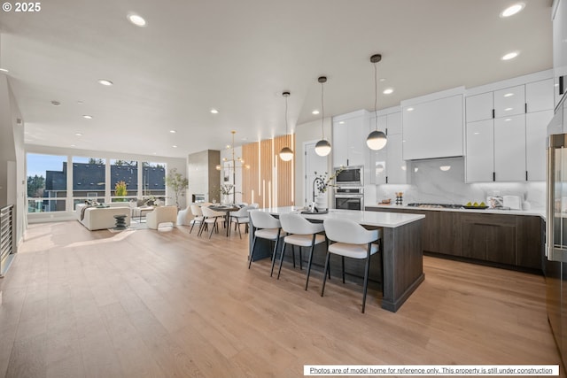 kitchen with a kitchen island with sink, stainless steel appliances, white cabinets, light hardwood / wood-style flooring, and decorative light fixtures