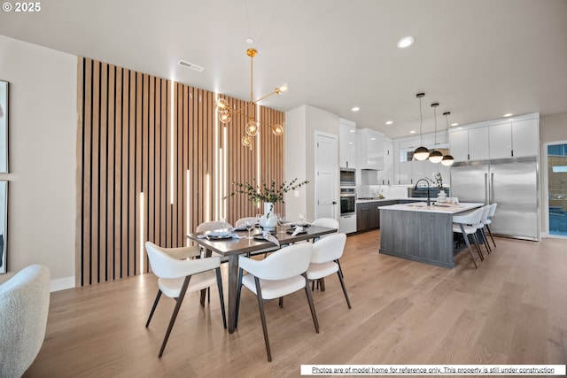 dining room with sink, a chandelier, and light hardwood / wood-style floors