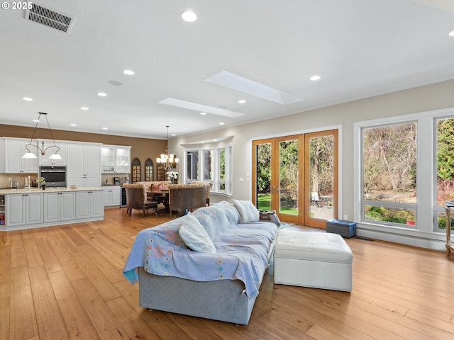 living area with a skylight, visible vents, light wood finished floors, and a chandelier