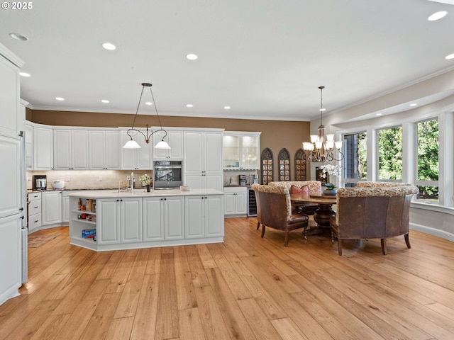 kitchen with a kitchen island with sink, a sink, ornamental molding, stainless steel oven, and backsplash