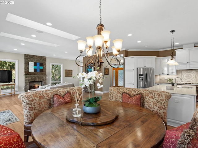 dining room featuring baseboards, light wood-style flooring, a skylight, recessed lighting, and a fireplace