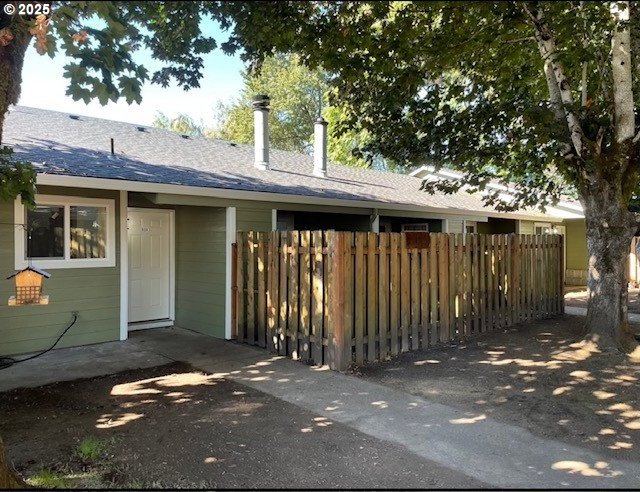 rear view of house with a shingled roof and fence