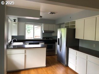 7922 SW Capitol Hill Rd, Portland, OR 97219 - kitchen with stainless steel appliances, dark countertops, a sink, light wood-type flooring, and a peninsula