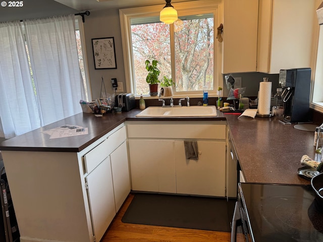7922 SW Capitol Hill Rd, Portland, OR 97219 - kitchen with a sink, dark countertops, a peninsula, white cabinetry, and black / electric stove
