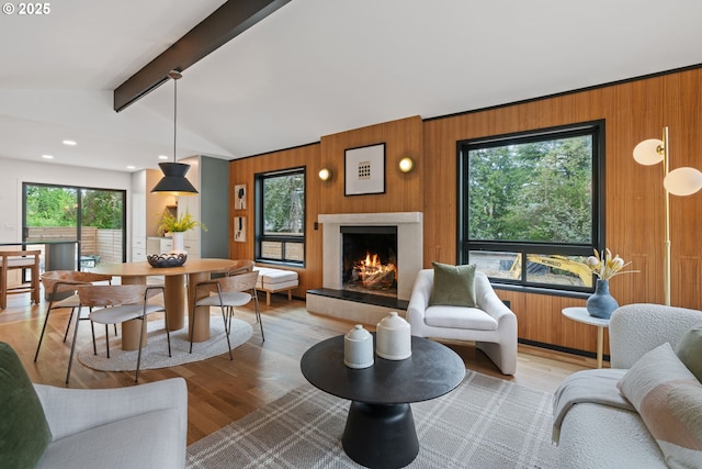 living area featuring wooden walls, a warm lit fireplace, light wood-type flooring, and recessed lighting