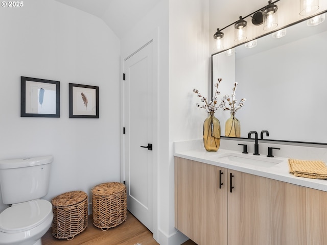 bathroom with wood-type flooring, toilet, vanity, and lofted ceiling