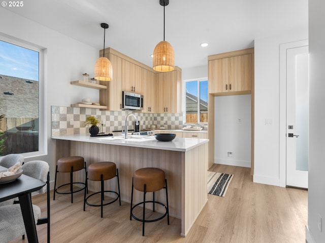 kitchen with kitchen peninsula, pendant lighting, light brown cabinetry, light wood-type flooring, and tasteful backsplash