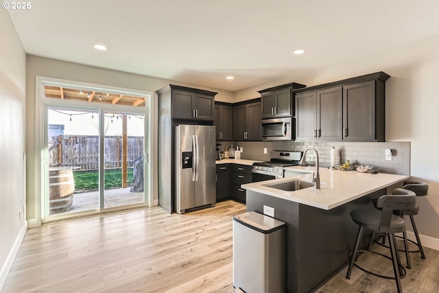 kitchen featuring a kitchen bar, sink, light hardwood / wood-style flooring, stainless steel appliances, and backsplash