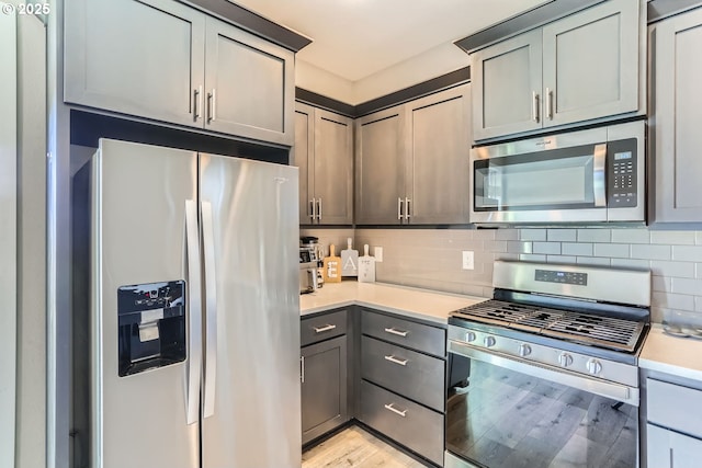 kitchen with gray cabinetry, stainless steel appliances, light hardwood / wood-style floors, and backsplash