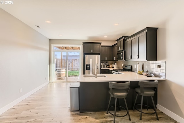 kitchen featuring tasteful backsplash, appliances with stainless steel finishes, light wood-type flooring, and kitchen peninsula