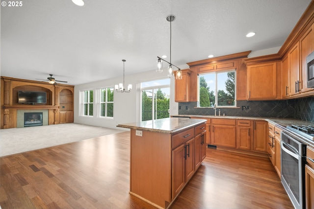 2530 NW 22nd Ave, Camas, WA 98607 - kitchen with oven, open floor plan, a ceiling fan, a glass covered fireplace, and wood finished floors