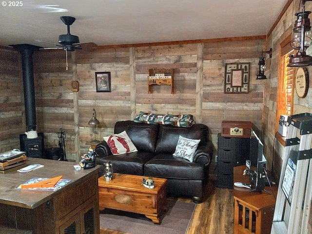 living area featuring a wood stove, wood walls, ceiling fan, and wood finished floors