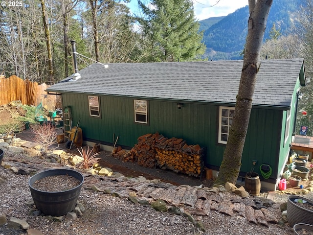 view of property exterior with an outbuilding, roof with shingles, fence, and a mountain view