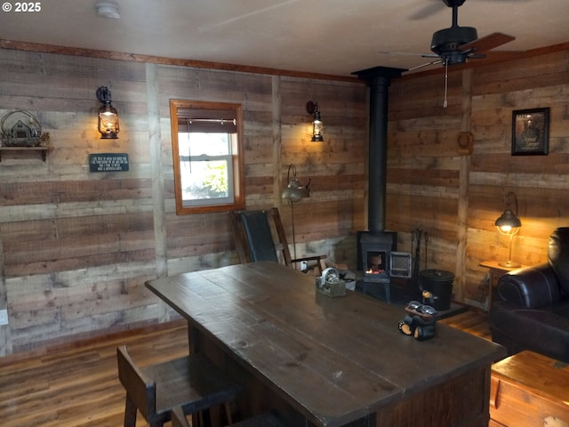 office with a wood stove, ceiling fan, wooden walls, and wood finished floors