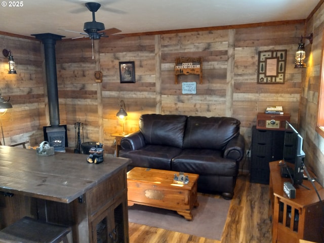 living area with a wood stove, wood walls, ceiling fan, and wood finished floors