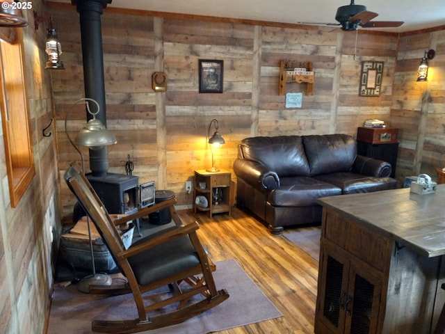 living room with a wood stove, ceiling fan, wooden walls, and wood finished floors