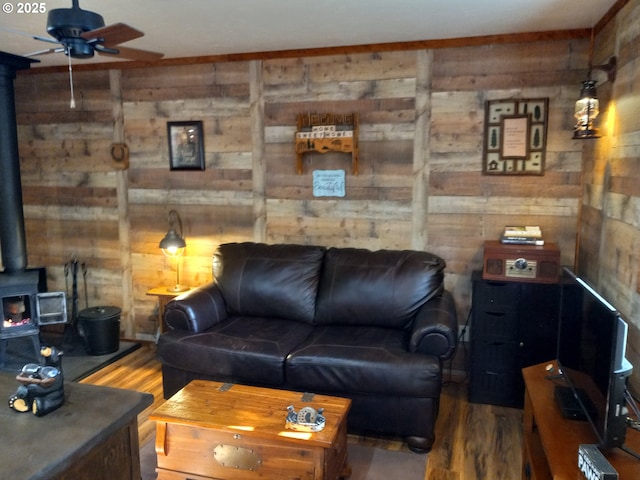 living area featuring a wood stove, wood walls, ceiling fan, and wood finished floors