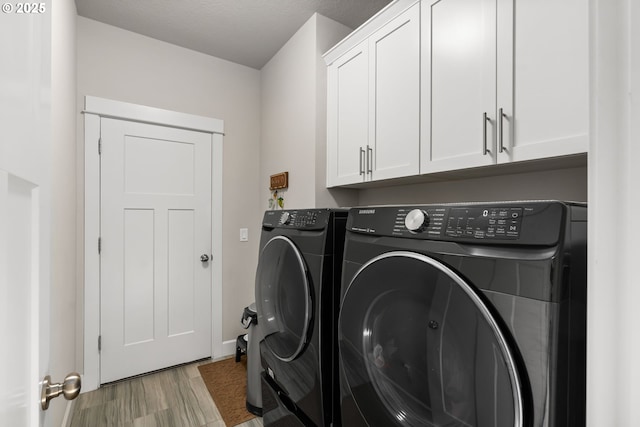 laundry room featuring cabinets, washing machine and clothes dryer, and light wood-type flooring