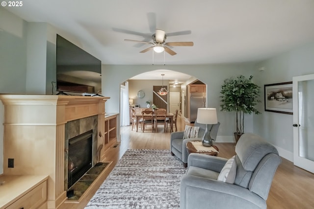 living room featuring wood finished floors, baseboards, arched walkways, ceiling fan, and a tiled fireplace