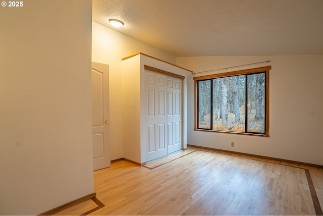 unfurnished bedroom with lofted ceiling, light hardwood / wood-style floors, a closet, and a textured ceiling