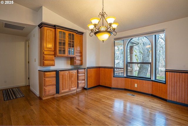 kitchen featuring pendant lighting, wooden walls, lofted ceiling, light hardwood / wood-style floors, and an inviting chandelier