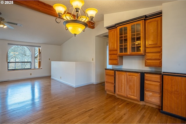 kitchen featuring ceiling fan with notable chandelier, lofted ceiling with beams, dark stone countertops, hanging light fixtures, and light wood-type flooring