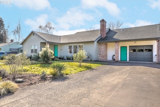 single story home with aphalt driveway, brick siding, a chimney, a front yard, and a garage