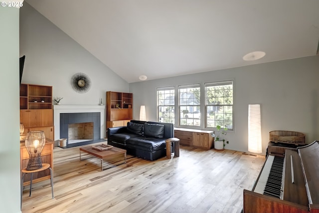 living room featuring high vaulted ceiling, a tile fireplace, and light wood-style flooring