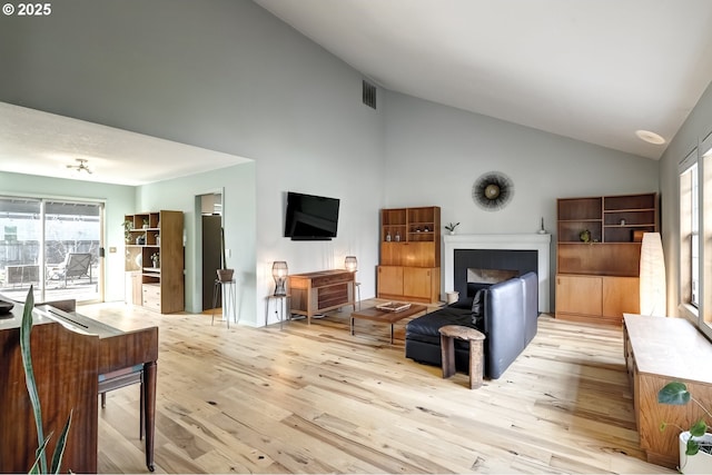 living room featuring high vaulted ceiling, a fireplace, visible vents, and light wood-style floors