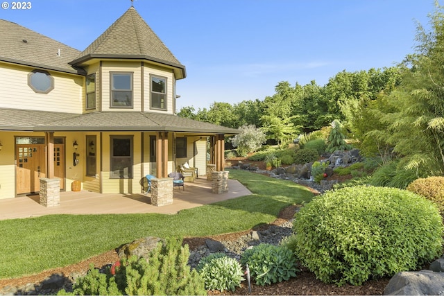 rear view of property with roof with shingles, a lawn, and a patio area