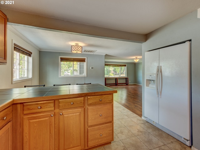 kitchen featuring tile countertops, white refrigerator with ice dispenser, open floor plan, and a wealth of natural light