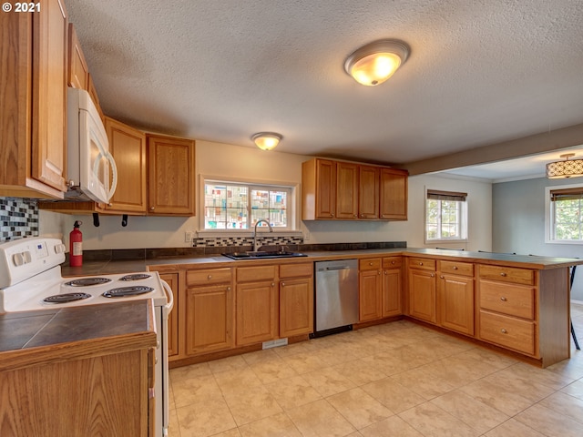 kitchen featuring a textured ceiling, a peninsula, white appliances, a sink, and tile counters