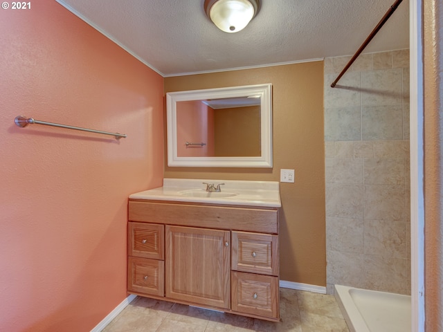 full bathroom featuring a textured ceiling, tiled shower, vanity, and baseboards