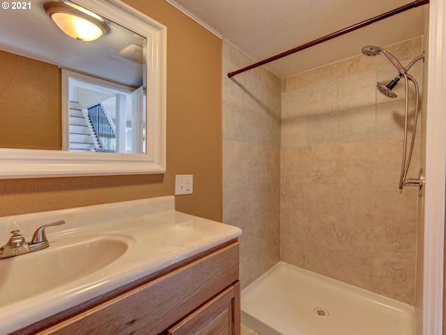 bathroom with a textured ceiling, a textured wall, a tile shower, and vanity