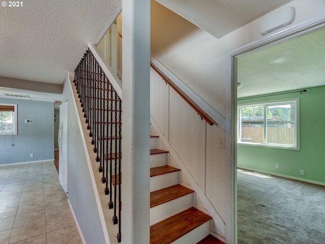 stairs with tile patterned flooring, plenty of natural light, a textured ceiling, and carpet