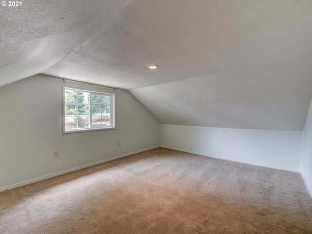 additional living space with a textured ceiling, carpet floors, vaulted ceiling, and baseboards