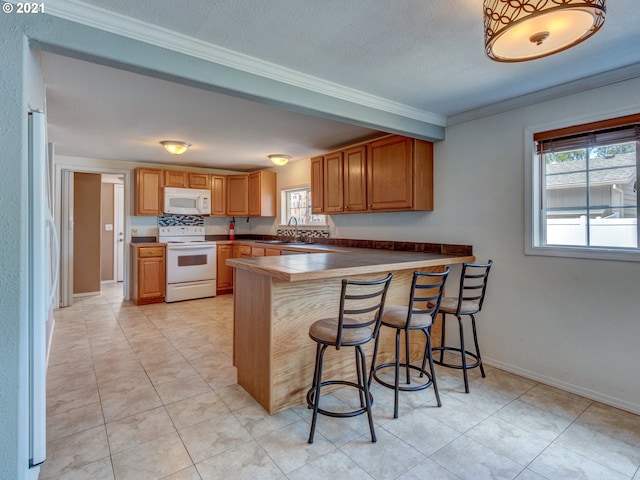 kitchen with a peninsula, white appliances, a breakfast bar, dark countertops, and crown molding